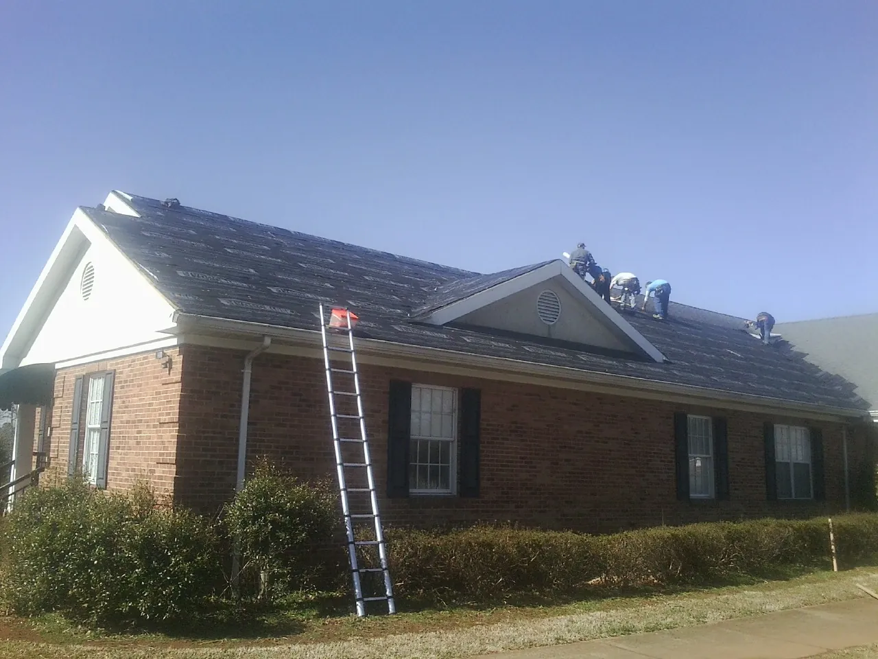 Crew tearing shingles off a brick ranch roof with a ladder set — Metal Roof Repair work by our crew in Uniondale