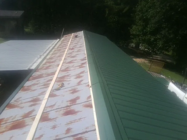 Old rusted panels beside newly installed green metal roofing — Wind Damage Roof Repair by Roofing Brothers in Uniondale