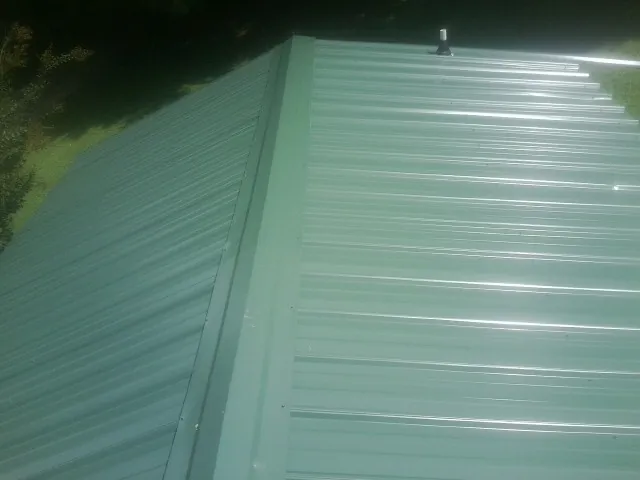 New green metal panels meeting at the ridge of a roof — Flat Roof Repair work by our crew in Uniondale