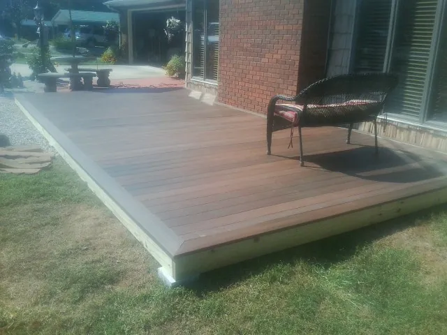 New wood deck and wicker chair beside a brick house in Uniondale